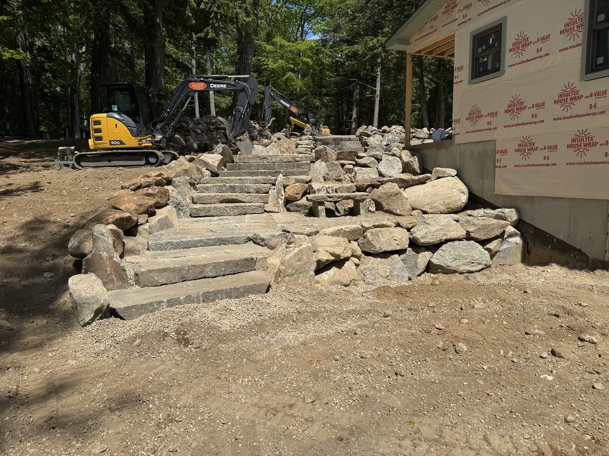 Excavator placing stone steps against a new home foundation