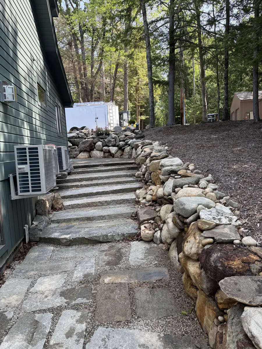 Stone slab steps climbing beside a home with rounded fieldstone border